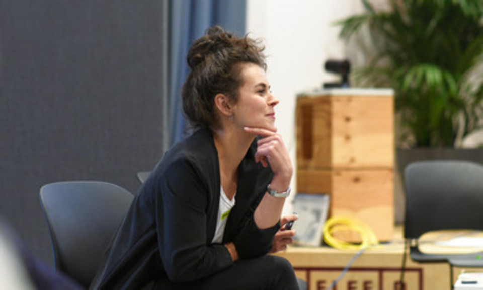 Reflexion beim Barcamp der Social Innovation Community Eine lächelnde Frau sitzt auf einem Stuhl und hat nachdenklich ihr Kinn auf die Hand gestützt